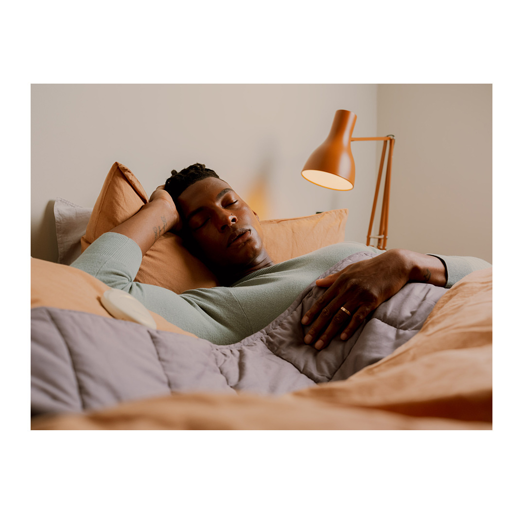 African-American man sleeping on bed with blanket and pillows next to lamp in bedroom. Indoor setting, relaxation concept.