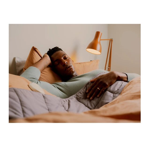 African-American man sleeping on bed with blanket and pillows next to lamp in bedroom. Indoor setting, relaxation concept.