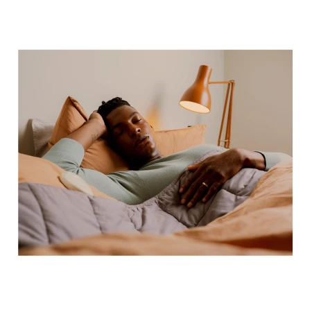 African-American man sleeping on bed with blanket and pillows next to lamp in bedroom. Indoor setting, relaxation concept.