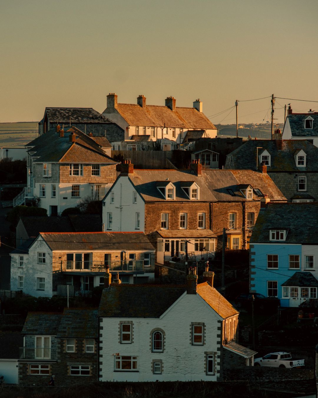 Residential neighbourhood in Cornwall, England with houses of varying heights and colors, captured during a sunny, golden hour.