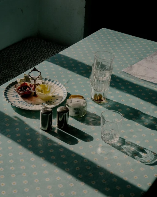 Overhead shot of a table with a patterned tablecloth, featuring a stack of drinking glasses, condiments, and a patterned plate with food.