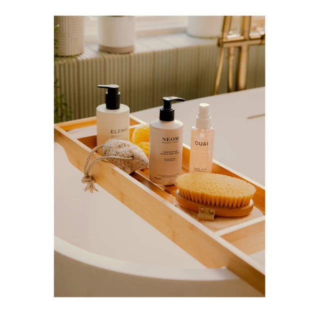 Bathroom still life featuring bath products on a wooden tray over a white tub, with a bright neutral color palette.