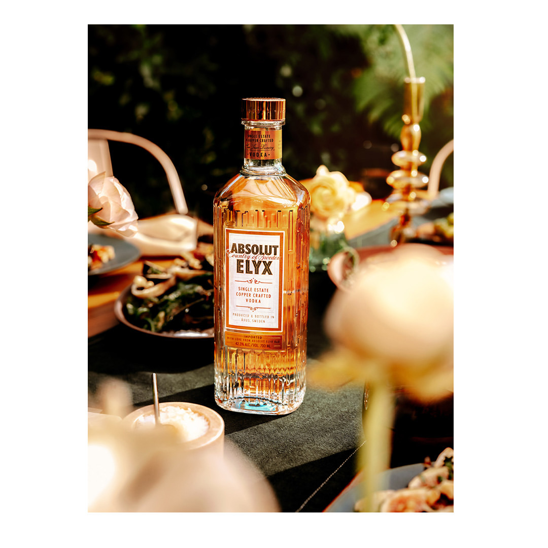 Bottle of Absolut Elyx vodka on a table with plates, flowers, and greenery creating an inviting atmosphere for a food and beverage setting.