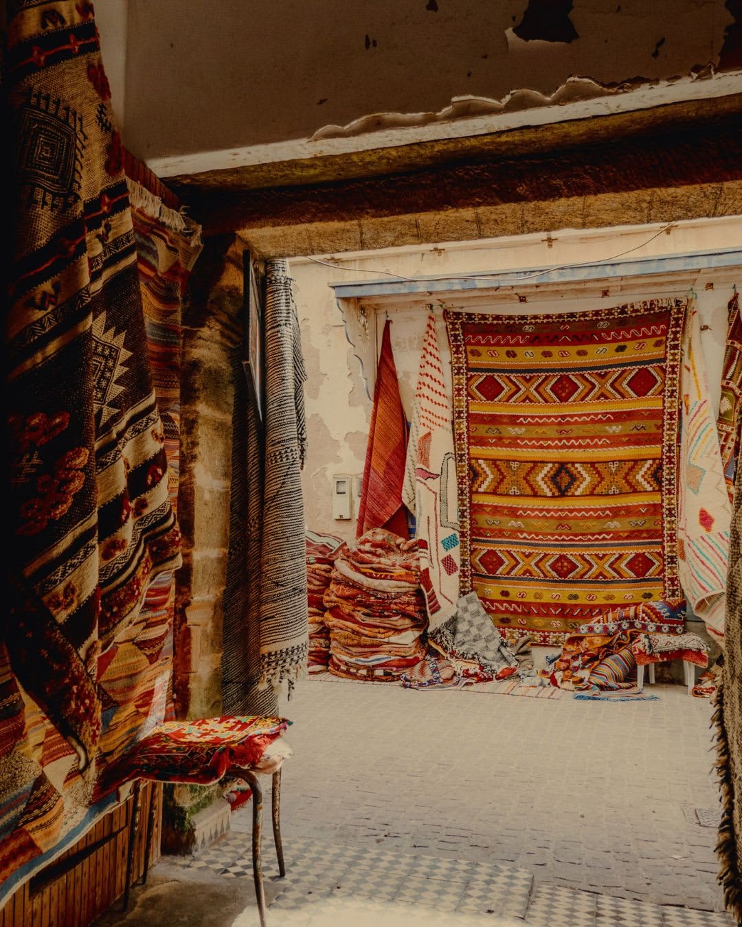 Display of various colorful rugs and textiles hanging in an indoor market, showcasing a variety of patterns and textures.