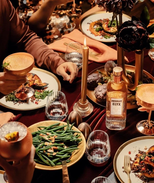 Overhead shot of a festive holiday feast with cocktails, vegetables, and a bottle of Elyx vodka on a burgundy velvet tablecloth.