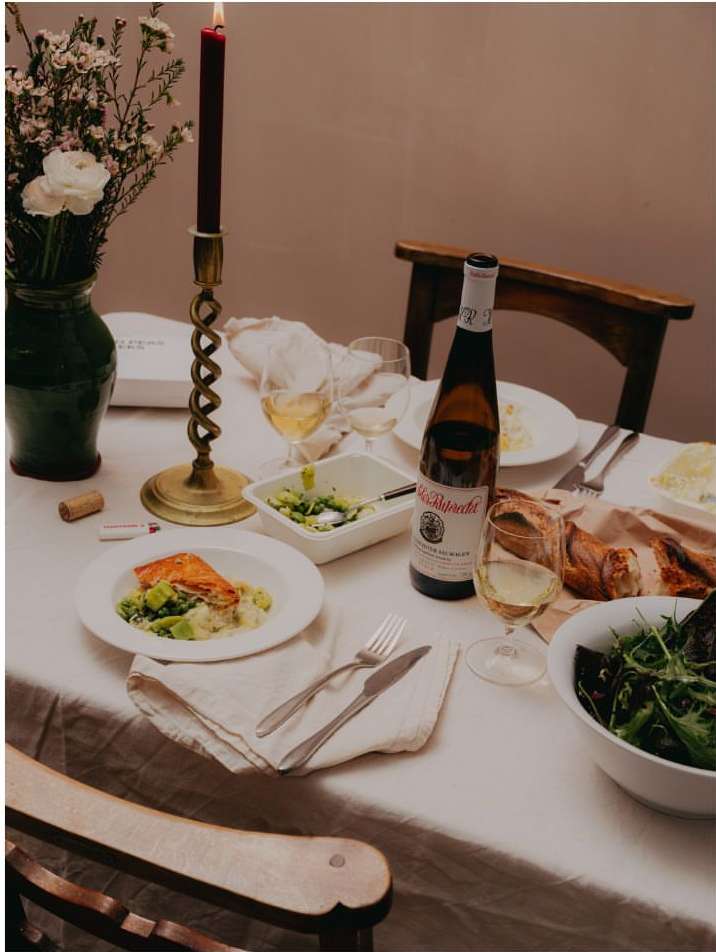 Elegant dinner table setting with salmon, wine, salad, flowers, and candlelight in a cozy indoor dining environment.