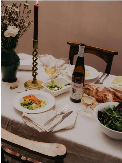 Elegant dinner table setting with salmon, wine, salad, flowers, and candlelight in a cozy indoor dining environment.