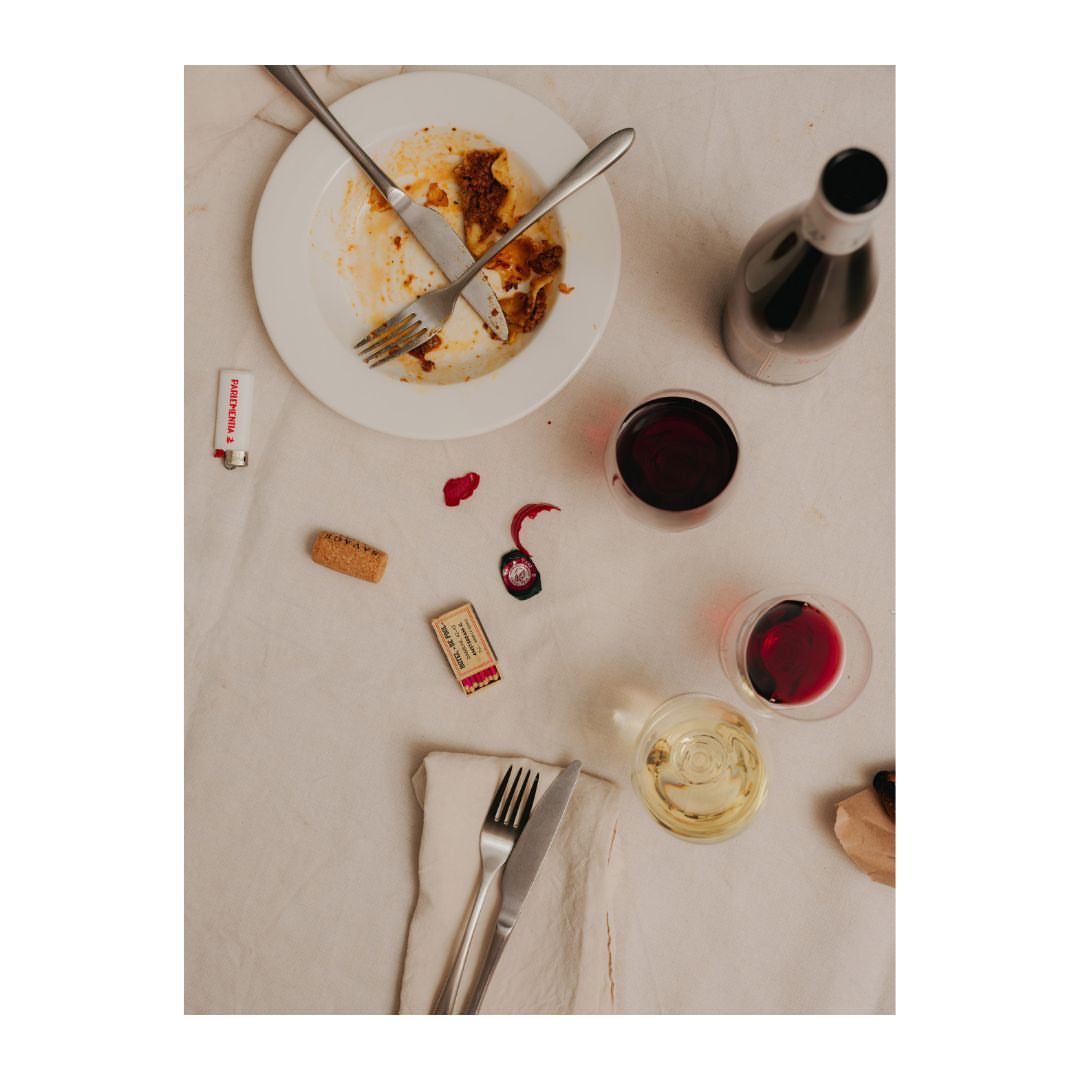 Overhead shot of a table setting with an empty plate, silverware, wine glasses with red and white wine, and a bottle of red wine.