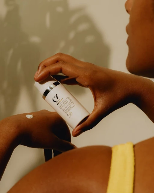 Person dispensing lotion from a white pump bottle onto their hand, set against a neutral background, in a skincare product shot.