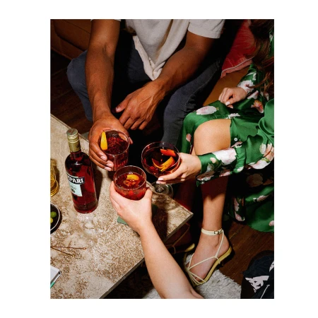 Three people holding cocktails around a table with a red bottle of Campari