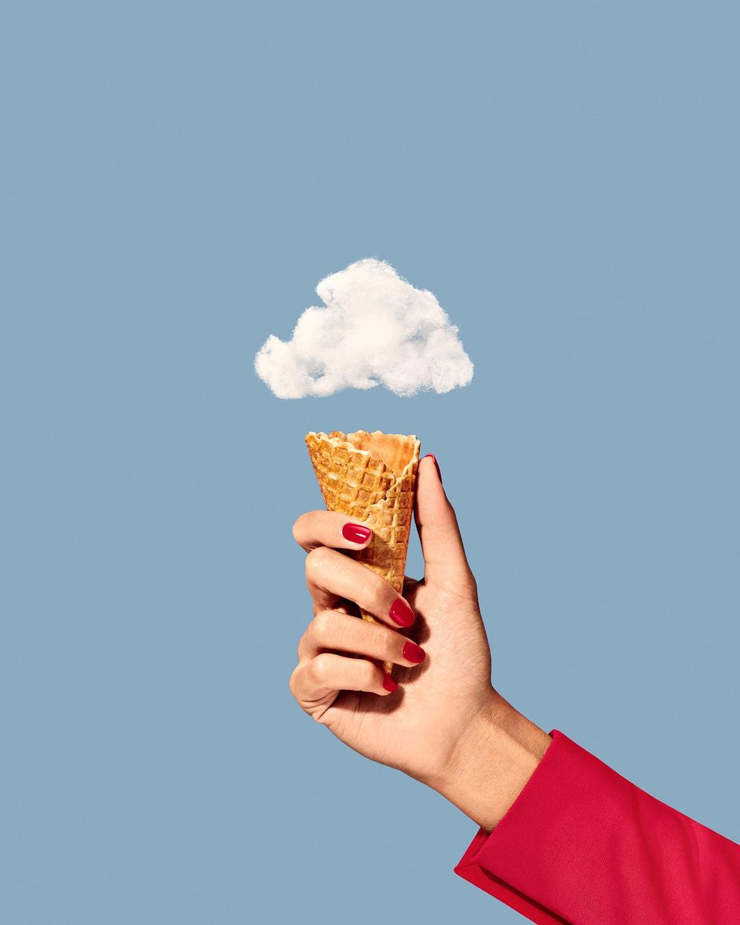 Conceptual food image: A woman's hand holds an ice cream cone with a cloud instead of ice cream against a light blue backdrop.