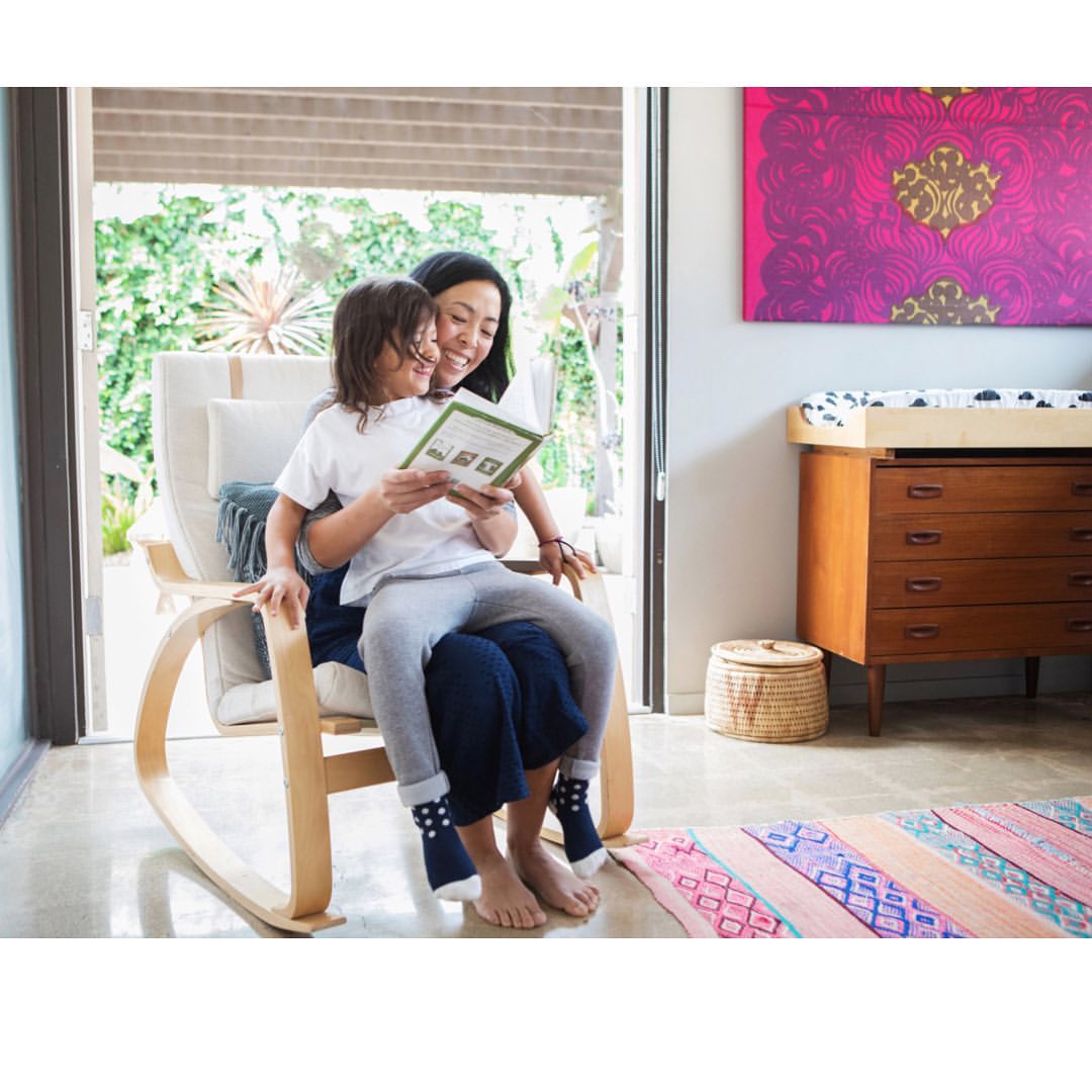 A happy mom and child share a book together sitting in a rocking chair inside a cozy home with modern decor and soft, natural lighting.