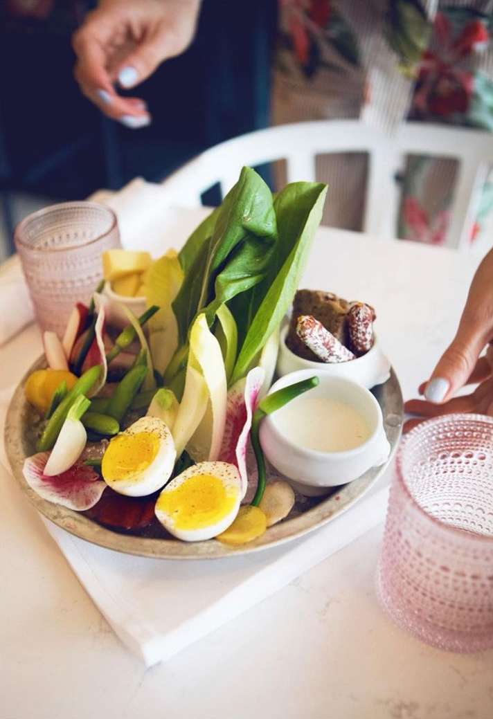 Overhead shot of a composed salad with greens, radishes, boiled eggs, and dipping sauce on a silver platter with a white background.