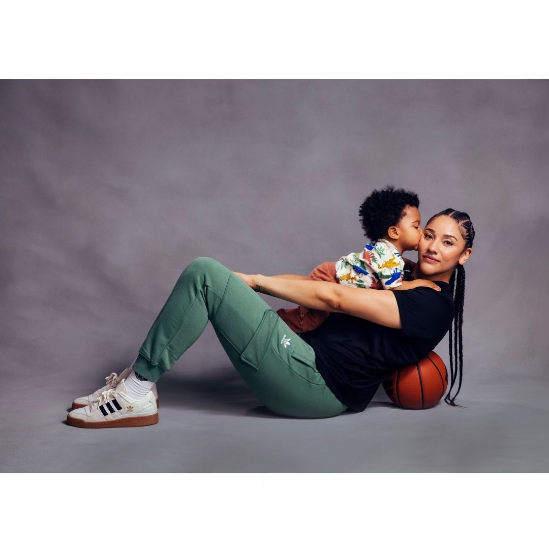 Woman and child pose indoors with basketball, both wearing Adidas athletic wear in a studio setting with grey background.