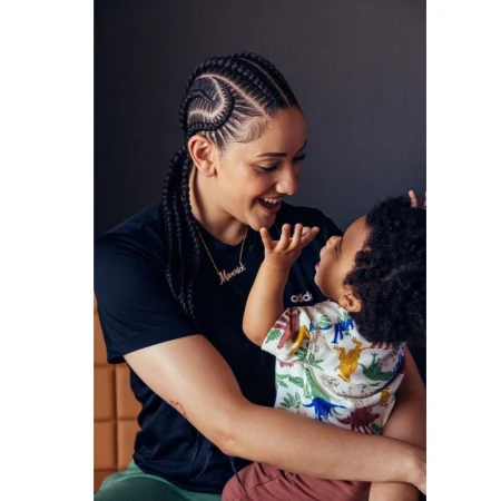 Woman with braided hair smiling at a toddler holding up a hand in a studio setting by Jennifer Roberts