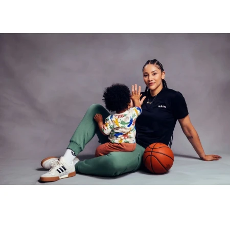 Woman in black t-shirt and green sweatpants seated on a grey seamless backdrop with a child and a basketball.