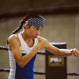 Female boxer wearing an American flag headband and a blue and white tank top inside a boxing ring, photographed by Jennifer Roberts.