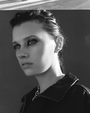 Monochrome portrait of a woman with dark smudged eye makeup wearing a dark jacket and chain necklace by Jeremy Choh