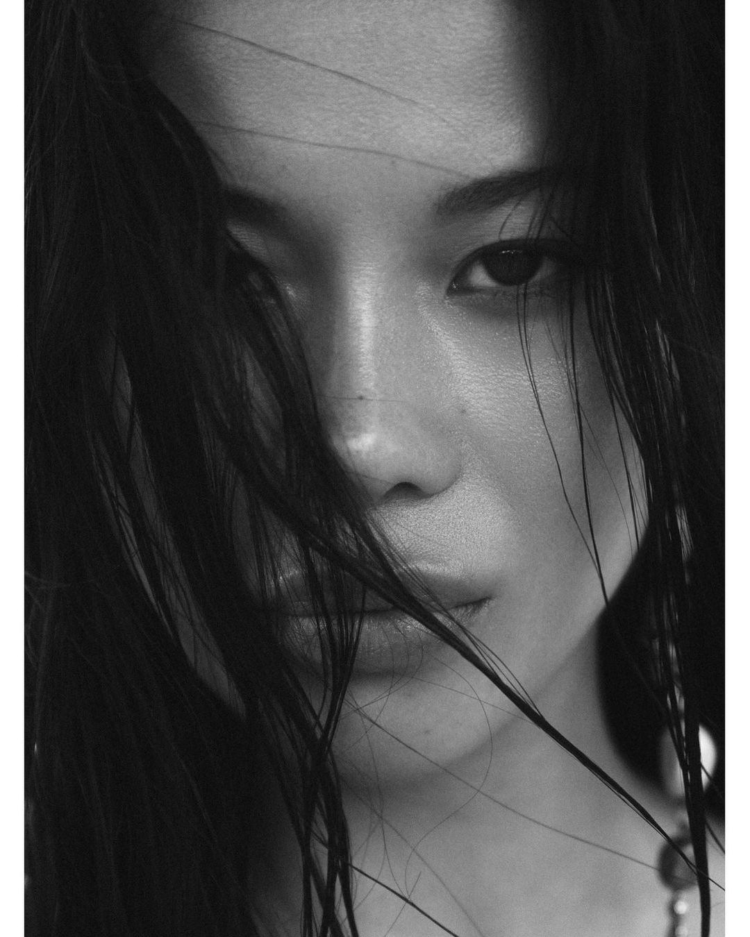 Monochrome close-up of an Asian woman with dark hair partially covering her face, creating an intimate and dramatic portrait.