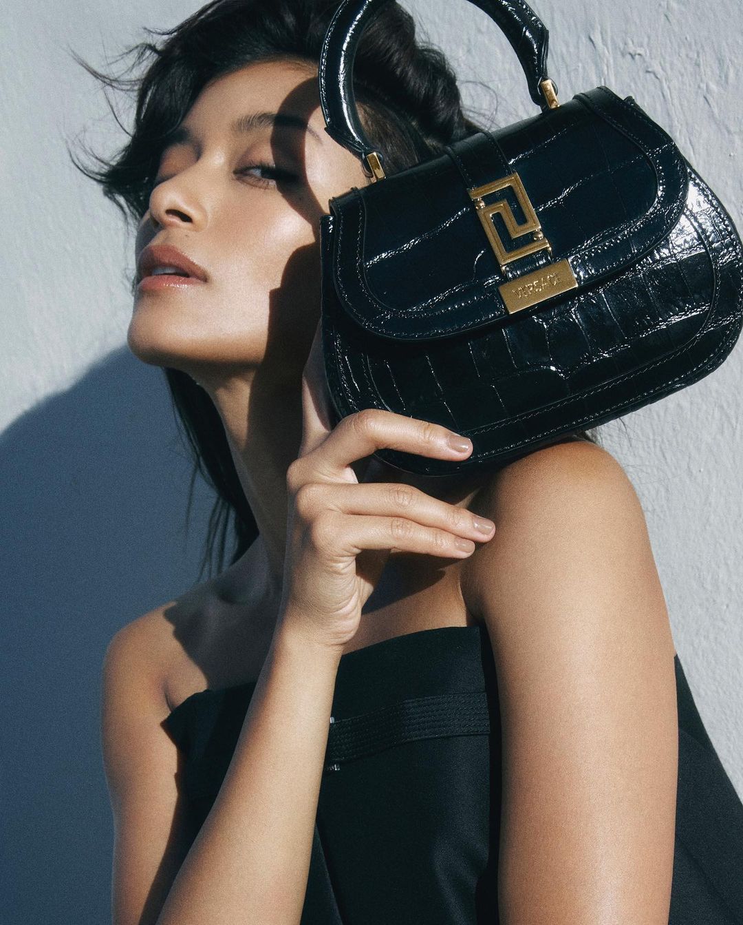 Elegant black crocodile-embossed top-handle bag held by a stylish adult woman in a studio setting.