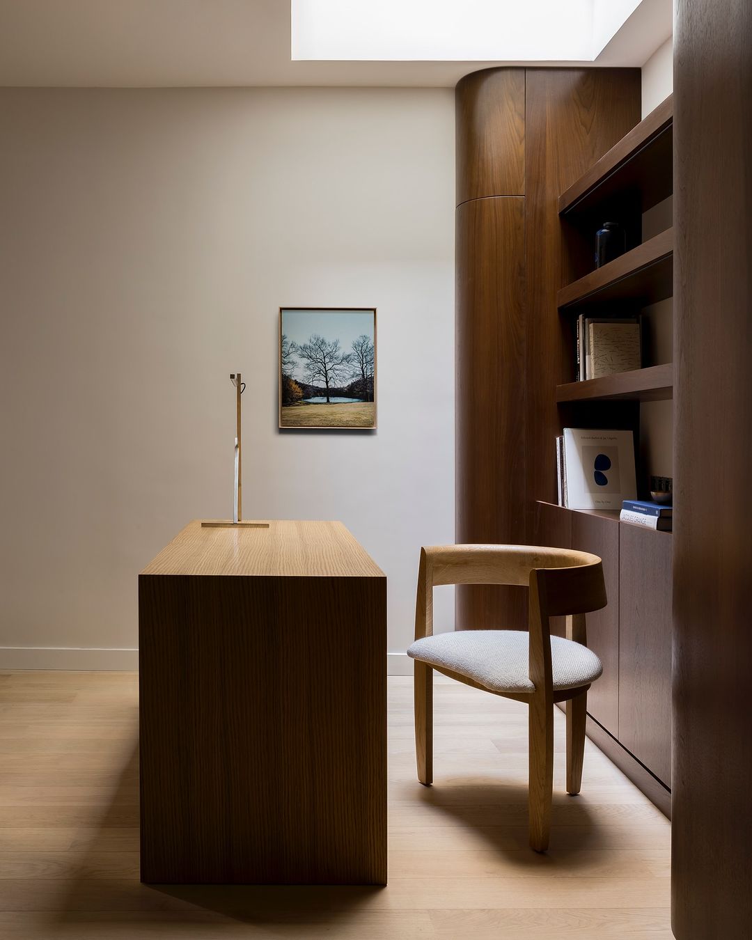 Minimalist home office interior with wooden desk, chair, built-in shelving, and artwork in warm, neutral tones, creating a serene workspace.