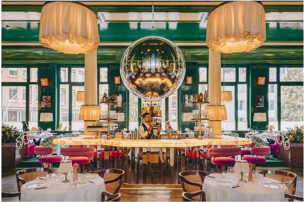 Upscale restaurant interior featuring a mirrored disco ball, seated tables with white linens, and a bartender behind a lighted bar.