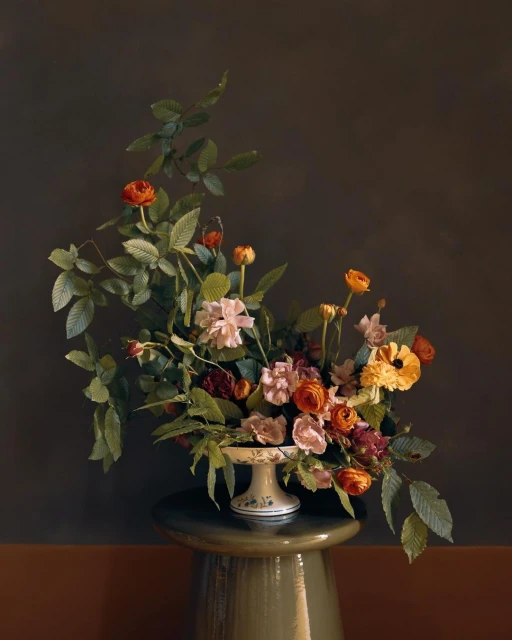 Floral arrangement featuring a variety of flowers including roses, ranunculus, and greenery, displayed on a cake stand atop a green stool.