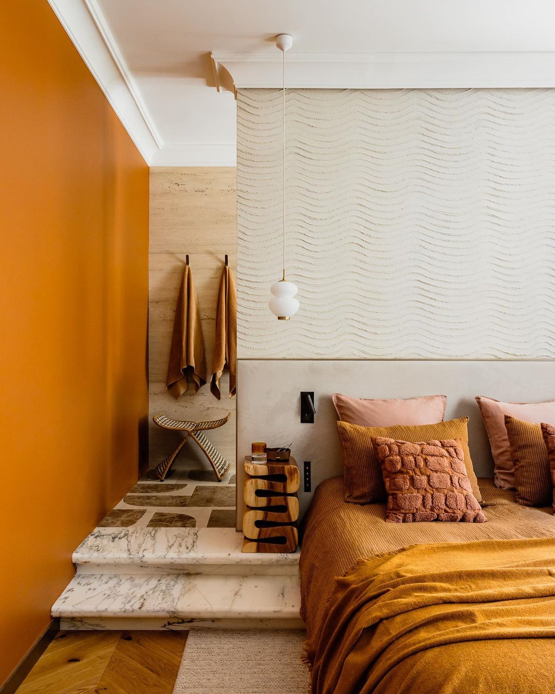 Cozy bedroom interior with warm orange and beige tones, featuring a made bed, marble steps, and modern lighting for a comfortable ambiance.
