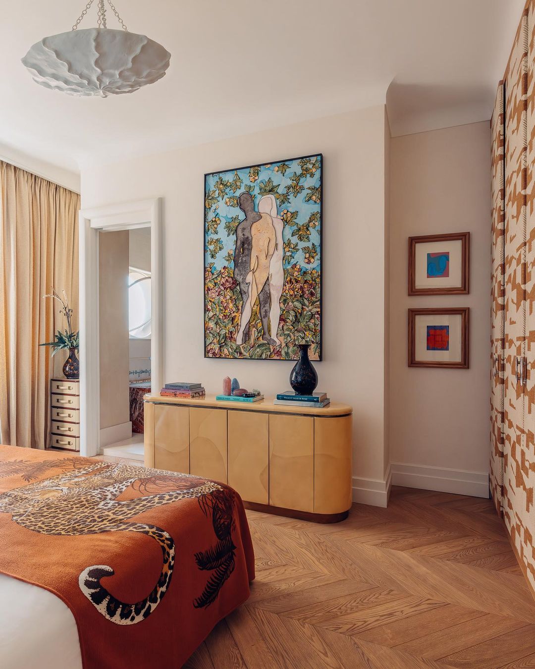 Interior view of bedroom featuring a tiger-print blanket, herringbone floors, neutral wall, and a modern art painting above a cabinet.