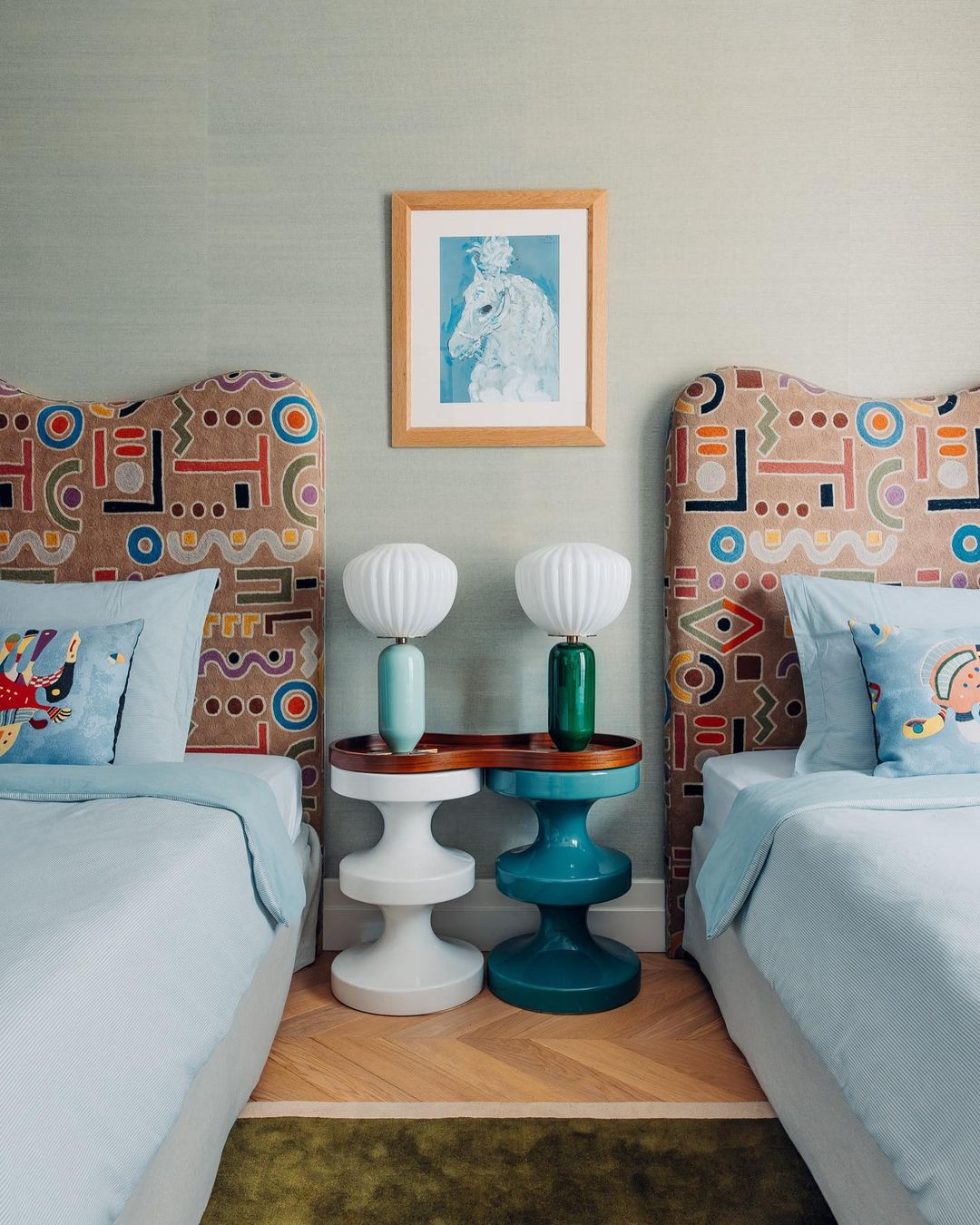 Interior of a bedroom featuring two beds with patterned headboards, matching blue linens, and unique side tables with lamps. 