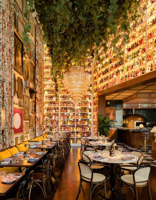 Upscale Italian restaurant interior with long tables, hanging plants, art-covered walls, chandelier, wine racks, and an inviting atmosphere.