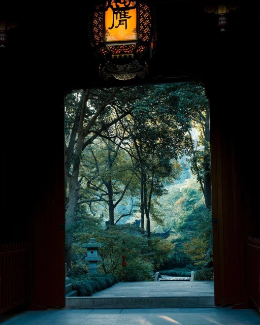 View through doorway with hanging lantern in the foreground to greenery and a traditional Asian building in the distance.