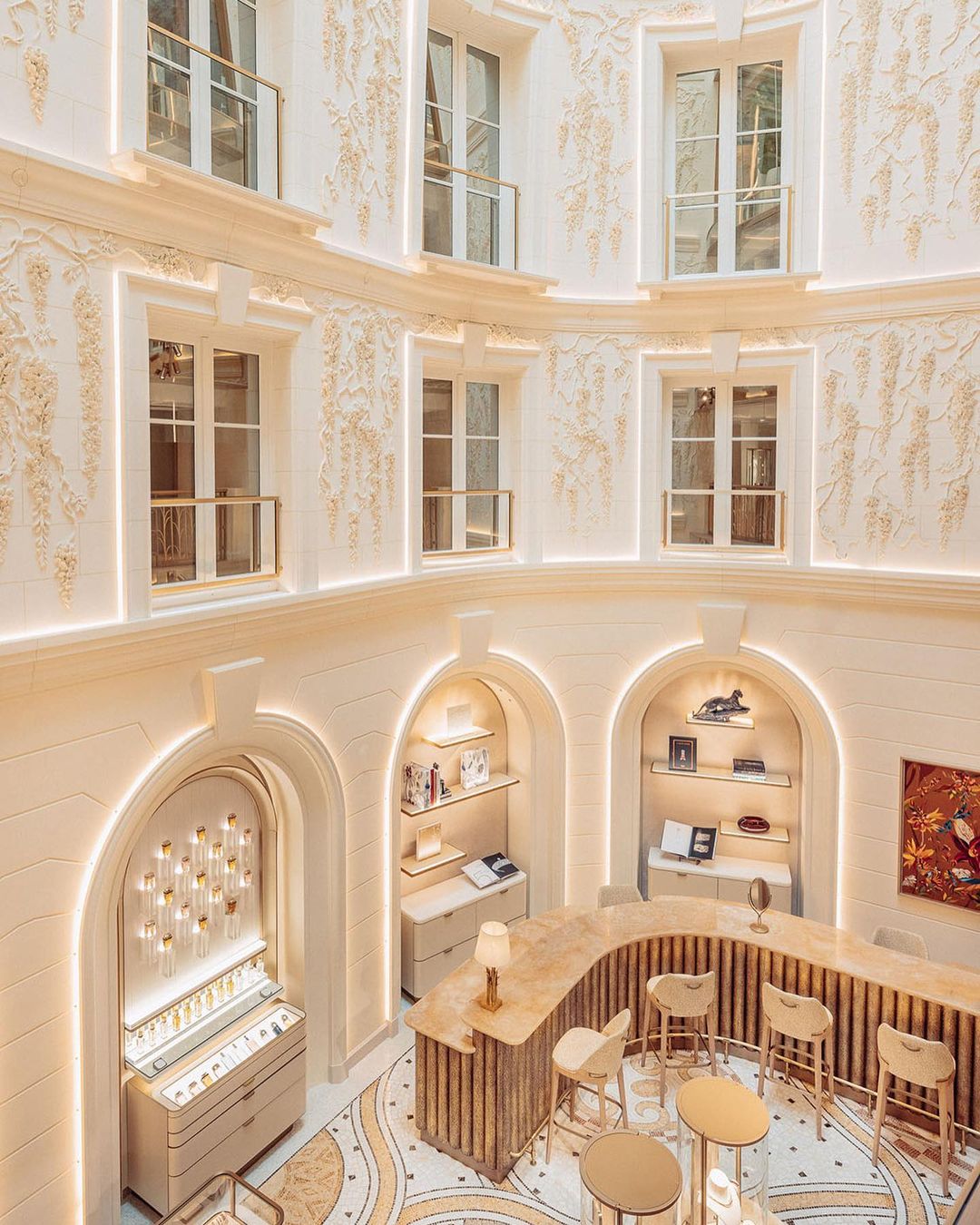 Interior of a boutique store with an ornate arched display, counters, and seating, illuminated by recessed lighting in a multi-story space.