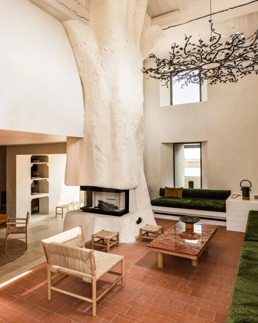 Indoor shot of a modern living room features a tree-shaped fireplace, rustic furniture, earthy color scheme, and a unique chandelier.