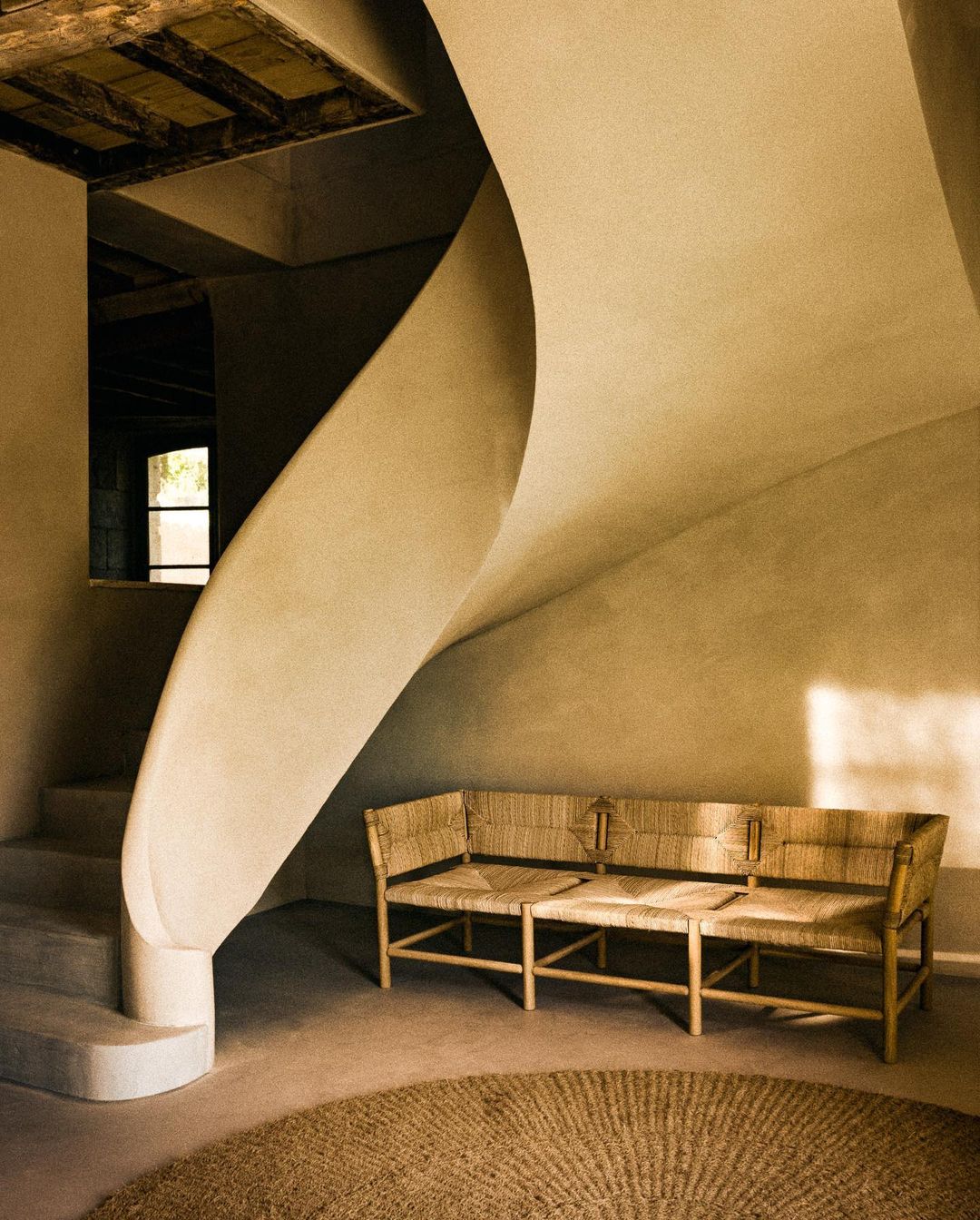 Interior space featuring a woven bench seat in front of a winding staircase, complemented by a jute rug on the floor.