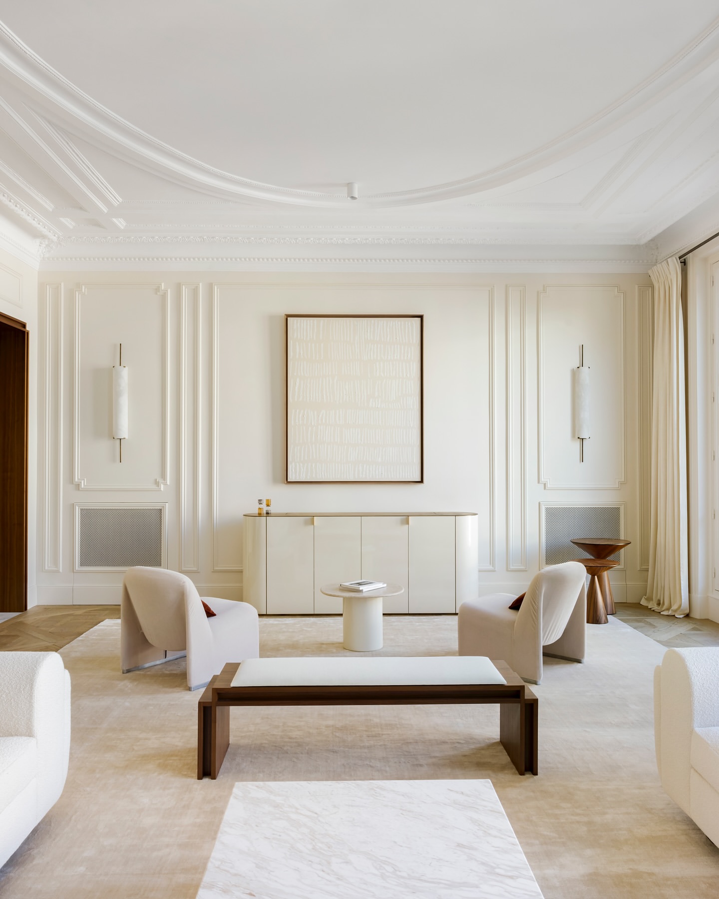 Bright and neutral living room with upholstered chairs, a marble coffee table, and an abstract art piece hanging on the wall.