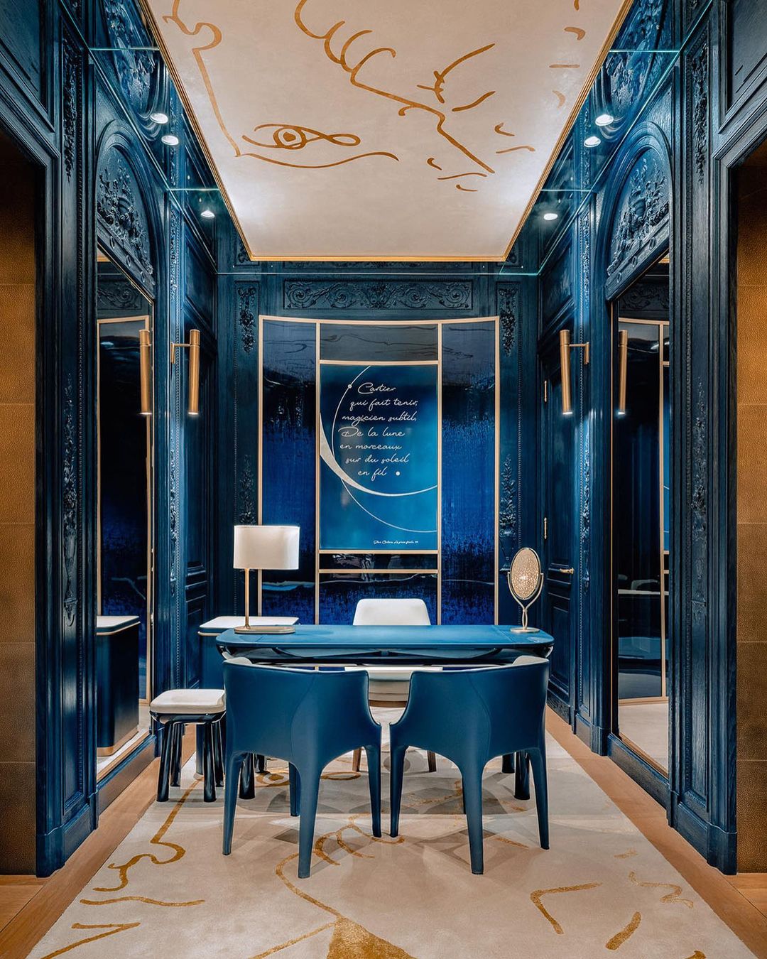 Sophisticated interior with teal walls, custom millwork, gold accents, modern blue chairs, and decorative ceiling art in neutral colors.
