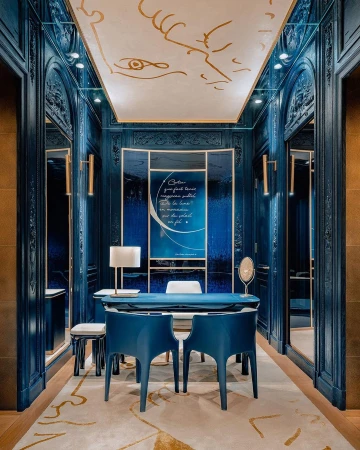 Sophisticated interior with teal walls, custom millwork, gold accents, modern blue chairs, and decorative ceiling art in neutral colors.