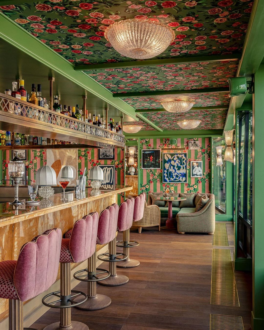 Interior of an ornate bar area, showcasing pink bar stools, a wooden bar, and decorative floral wallpaper and ceiling decor.