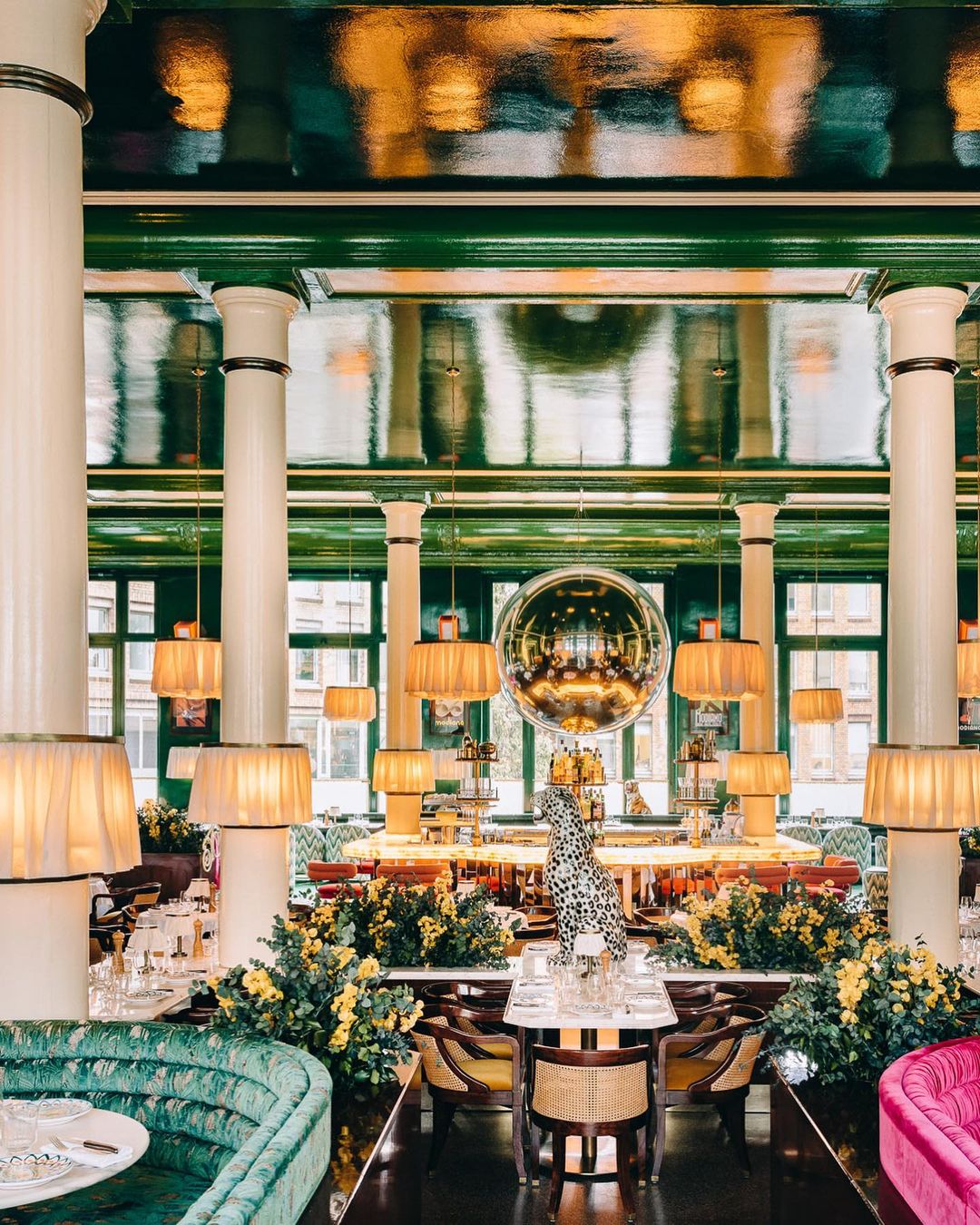 Ornate restaurant interior featuring green velvet booths, elegant table settings, yellow floral arrangements, and unique lighting fixtures.