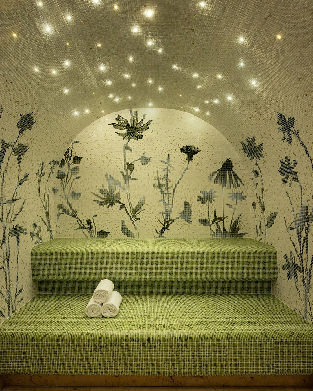 Relaxing spa interior featuring a tiled bench with rolled towels, floral-patterned walls, and a ceiling adorned with small, twinkling lights.