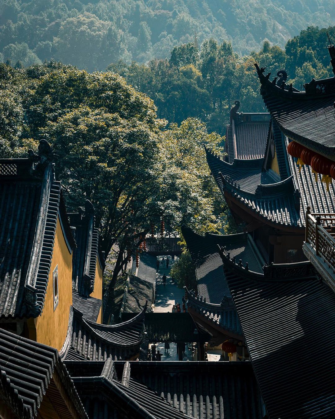 Chinese architecture featuring traditional tiered roofs and golden walls, set against a backdrop of lush, green mountains under natural light.