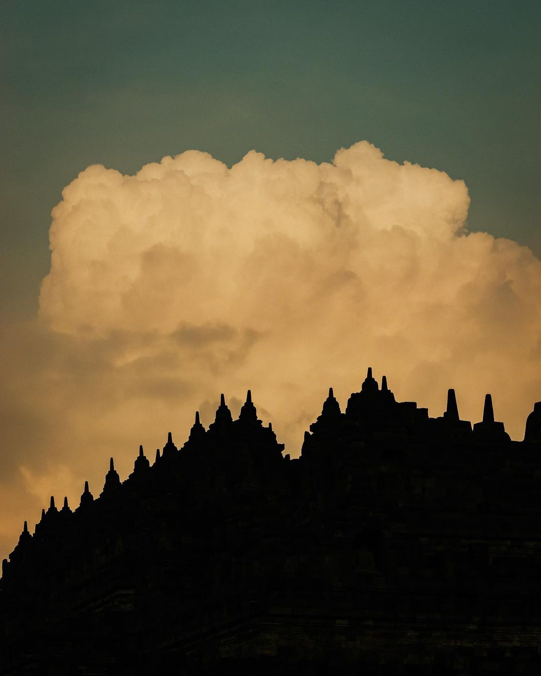 Silhouette of Borobudur temple against a cloudy sky at sunset, Indonesia. Ancient architecture and spiritual travel concept.