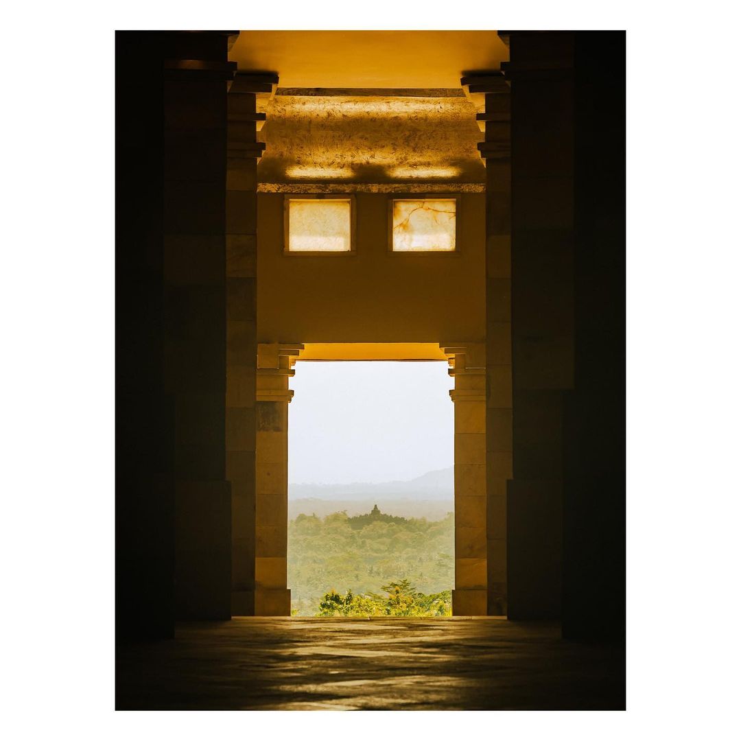 View through architectural columns of Borobudur temple in distance, Java, Indonesia. Sunlight highlights the columns and distant landscape.