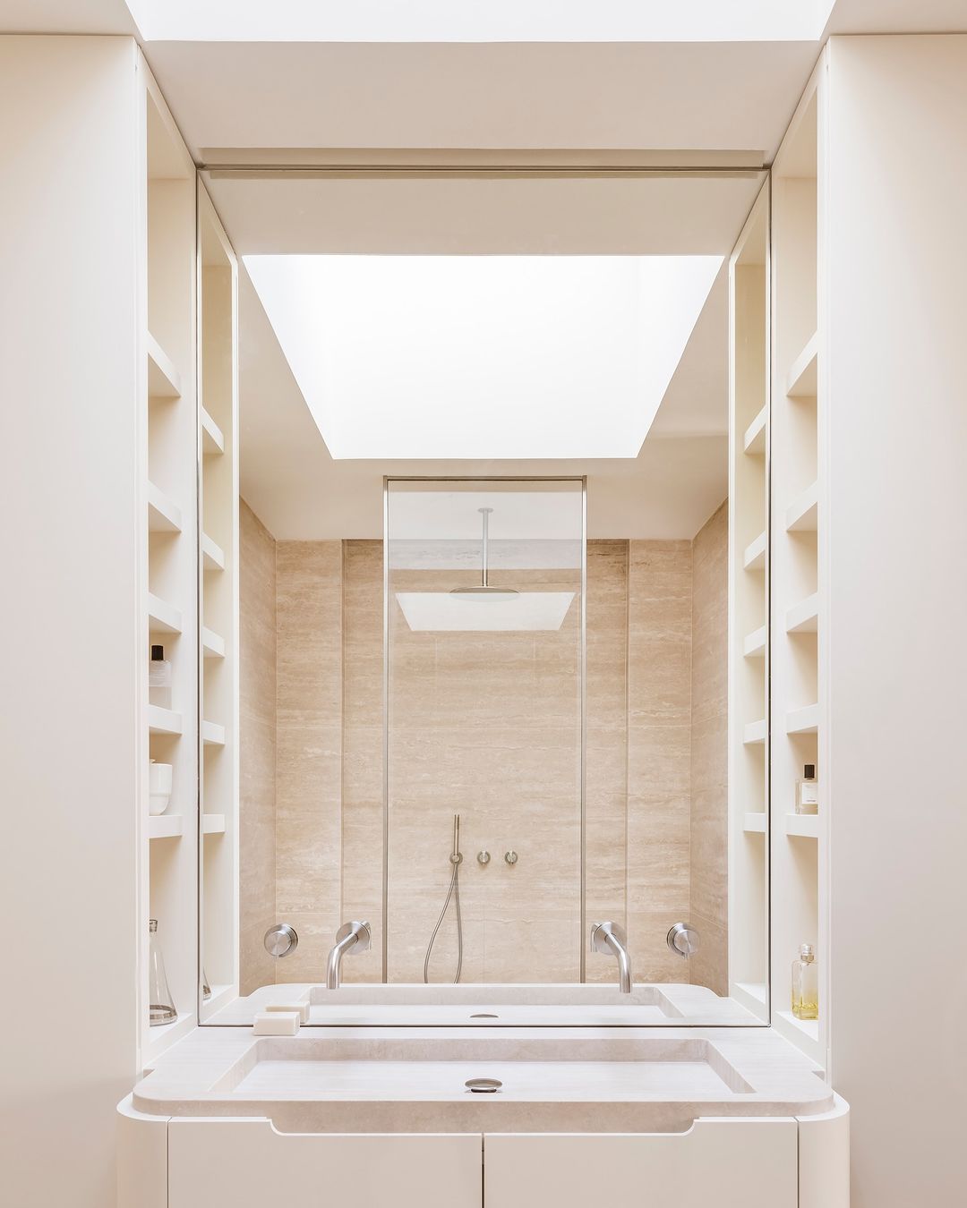 Modern bathroom interior featuring a double sink, mirrored wall, built-in shelving, neutral color palette, and natural light from a skylight.