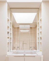 Symmetrical architectural interior photograph of a minimalist modern bathroom with built-in wall shelving and a stone sink.