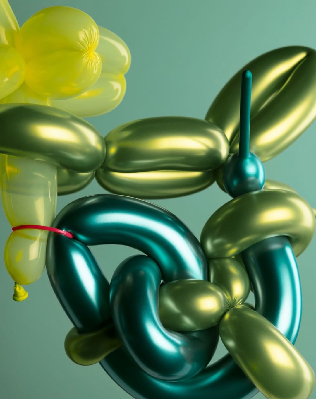 Sculptural balloon animal art piece in bright green and yellow tones on a seamless solid mint-green background. Modern style with creative design.