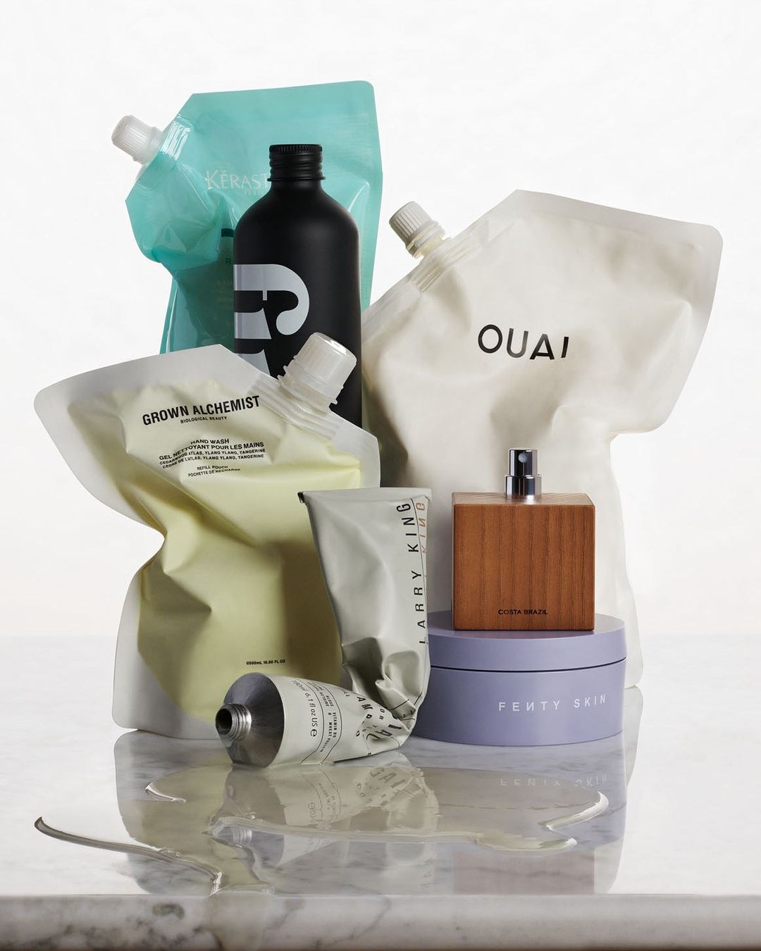 Still life of beauty and skincare products including bottles and tubes of creams and liquids on a marble surface against a white background.