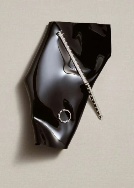 High-angle shot of black abstract shiny vinyl-like form, and a ring and bracelet on a white backdrop in a studio setting.