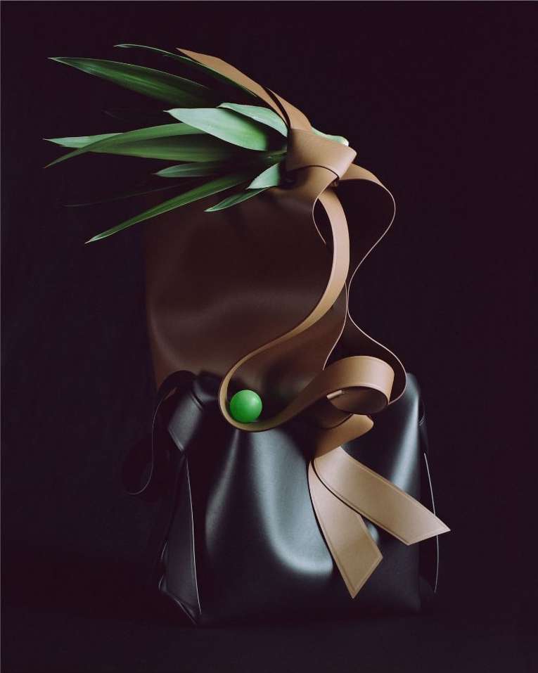 An artistic still life featuring a brown leather tote bag decorated with green leaves and a tan leather ribbon, against a dark background.